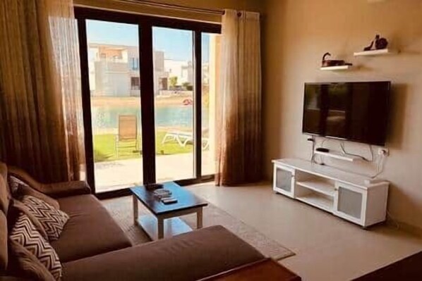 A living room with a sofa, a coffee table, a TV on a stand, and a sliding glass door leading to an outdoor area.
