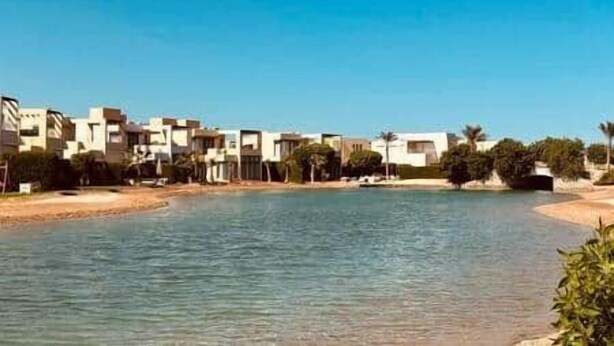 A coastal residential area with buildings along a waterfront, a sandy beach, and palm trees. - Sunset Haven in Tawila TownHouse (Hurghada)