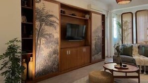 Un salon avec une grande armoire en bois, un téléviseur et une table basse ronde.
