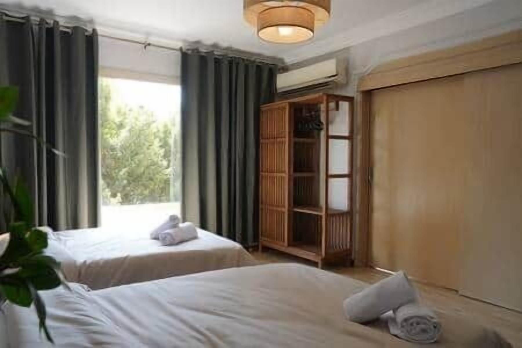 Hotellihuone, jossa on kaksi sänkyä, vaatekaappi ja ikkuna, jossa on verhot.