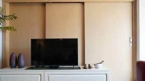 A flat-screen TV on a white cabinet with two vases and a small bowl.