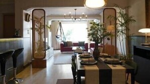 A dining area with a table set for four, a hanging light fixture above, and a sofa in the background.