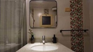 A bathroom with a marble sink, a mirror, a vase with flowers, and a shower curtain with a floral pattern.