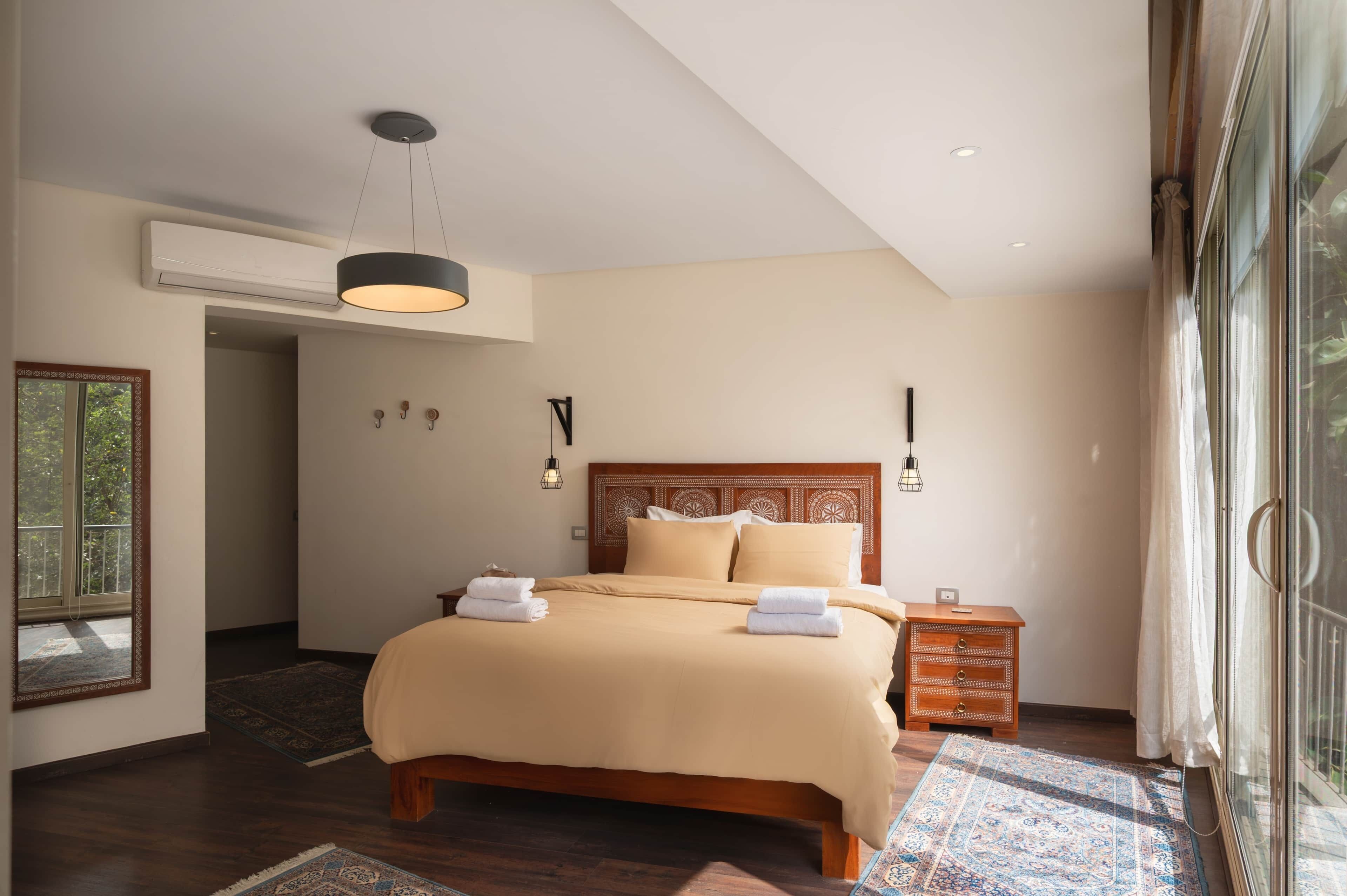 Une chambre d’hôtel moderne avec un grand lit, une table de chevet en bois, un miroir et une vue sur l’extérieur.