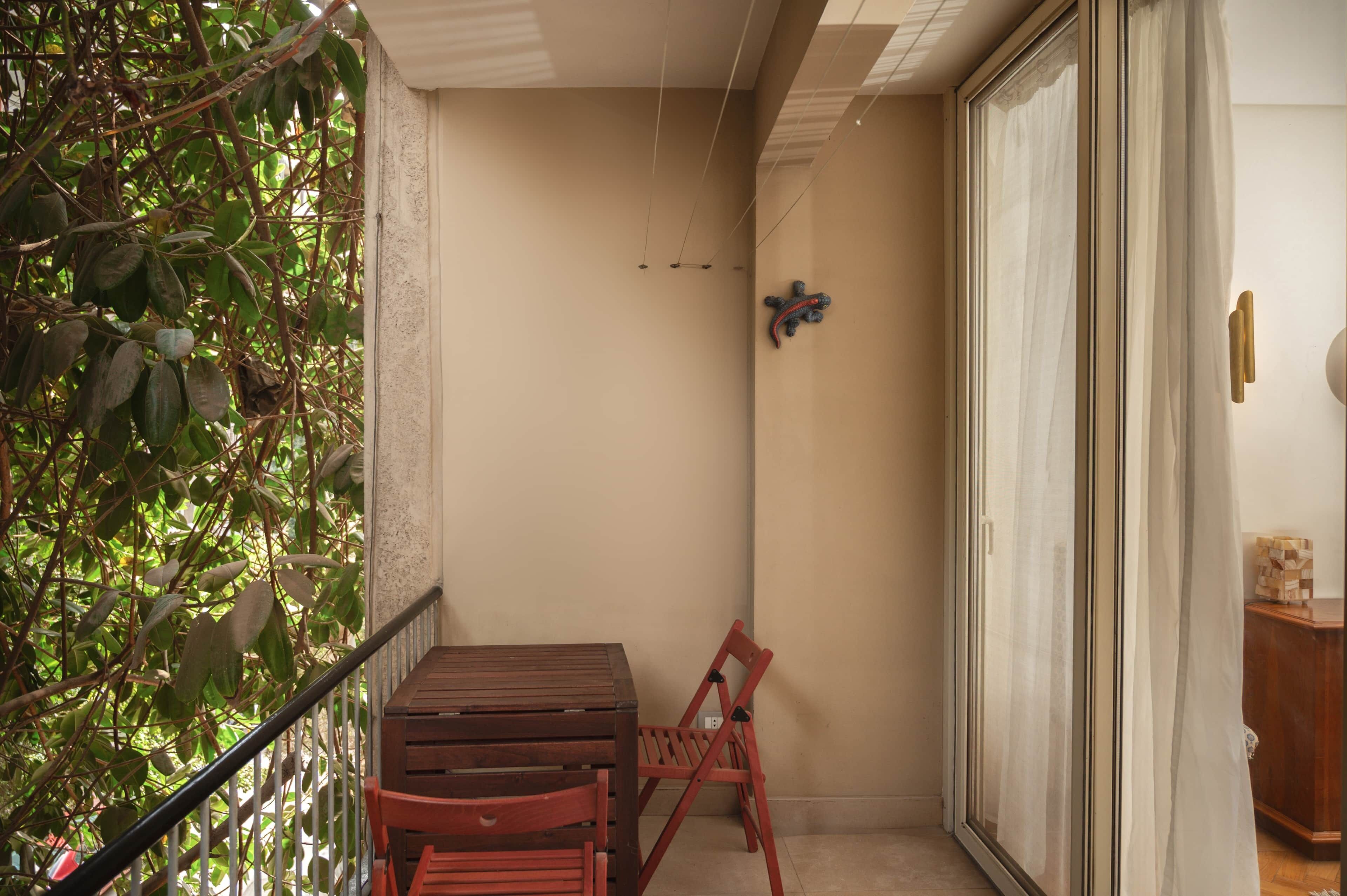 A balcony with a wooden table and two chairs, a potted plant, and a sliding glass door.