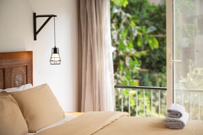 A bedroom with a bed, beige bedding, a hanging light fixture, a view of greenery through a window, and a balcony railing. - The Grand Tree House! (Cairo)