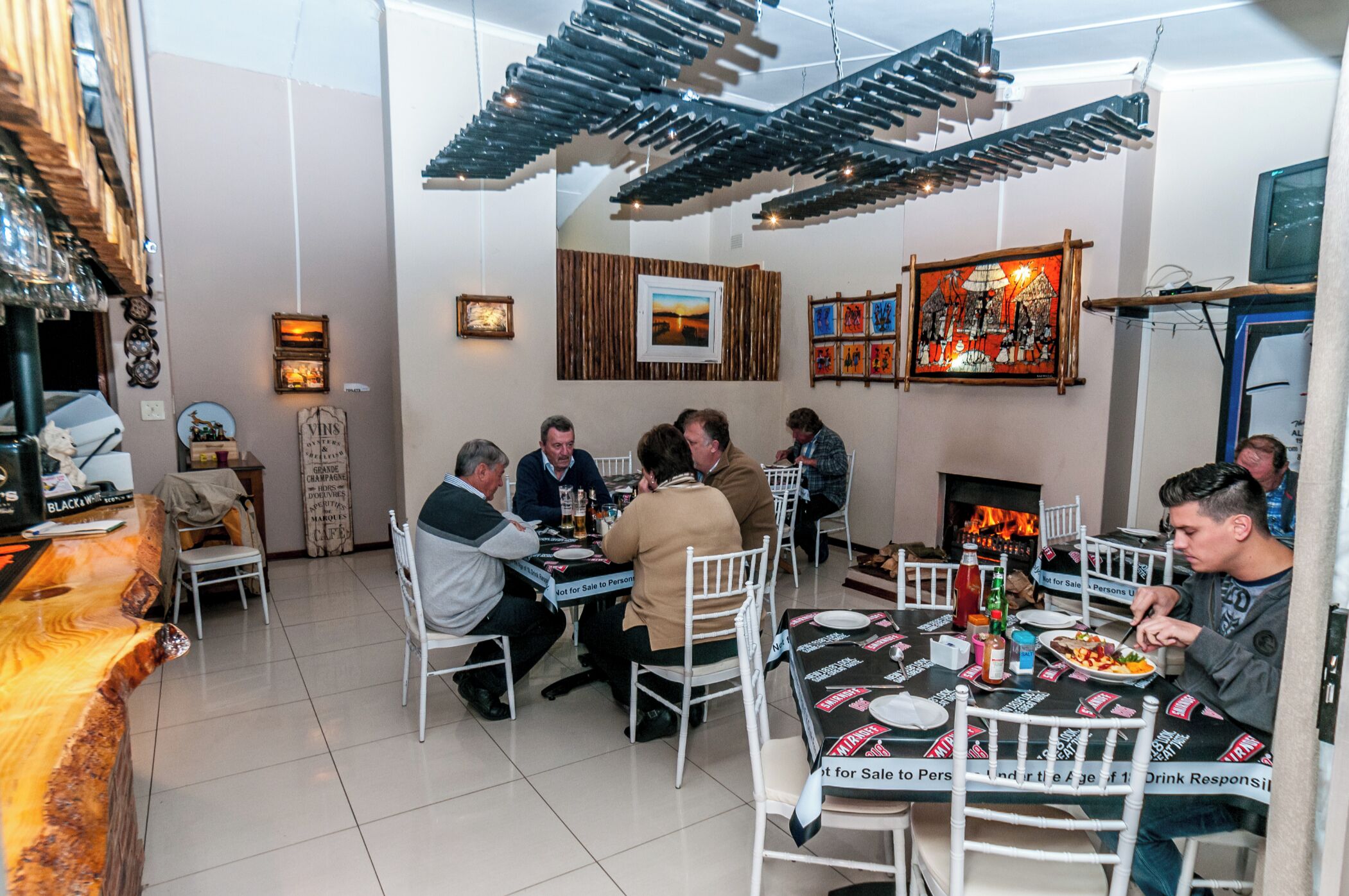 A restaurant with a long communal table, chairs, and a fireplace.
