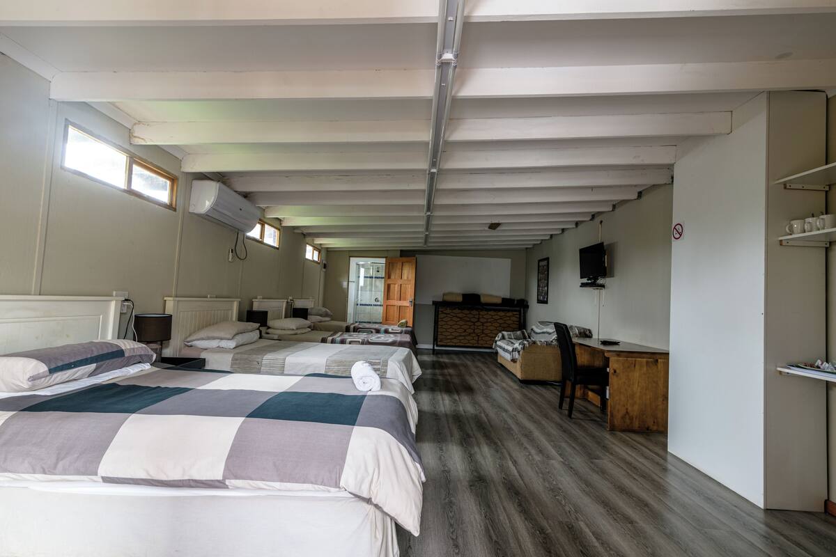 Ein Hotelzimmer mit zwei Betten, einem Schreibtisch, einem Sessel, einem Fernseher und einer kleinen Küchenzeile.
