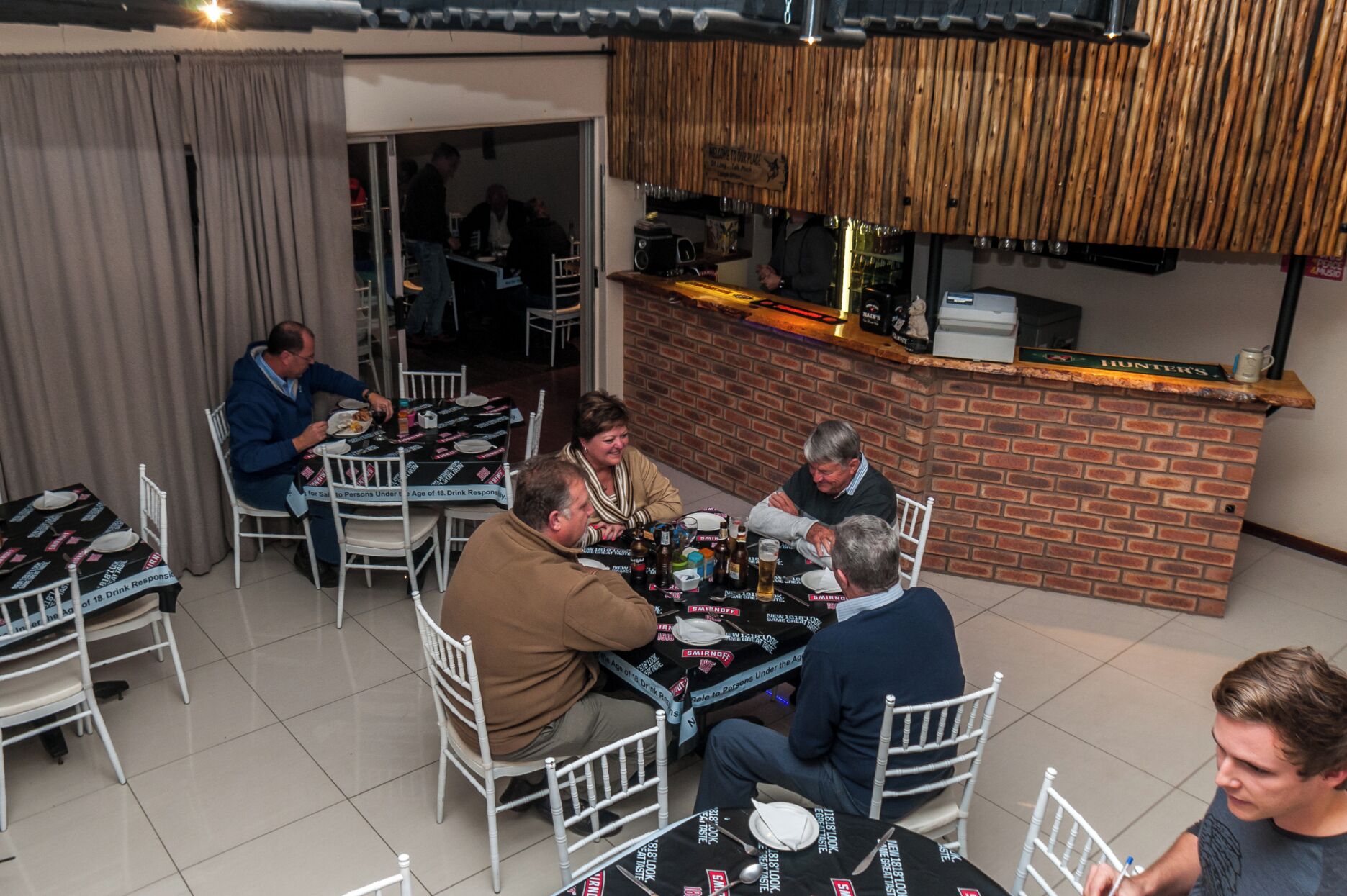 A group of people dining at a restaurant with a brick counter and white chairs.