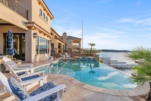 A swimming pool with lounge chairs, a view of the sea, and a building with balconies. - Splash Landing | Riverfront Estate with Infinity Pool, Guest House & Private Docks (Parker)