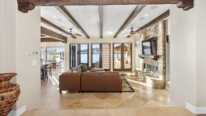 A spacious living area with a brown leather sofa, a stone fireplace, and a view of the outdoors. - Splash Landing |  Riverfront Estate with Infinity Pool, Guest House & Private Docks (Parker)