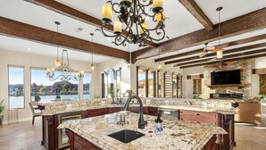 A spacious kitchen with a large island, granite countertops, and a stone fireplace. - Splash Landing |  Riverfront Estate with Infinity Pool, Guest House & Private Docks (Parker)
