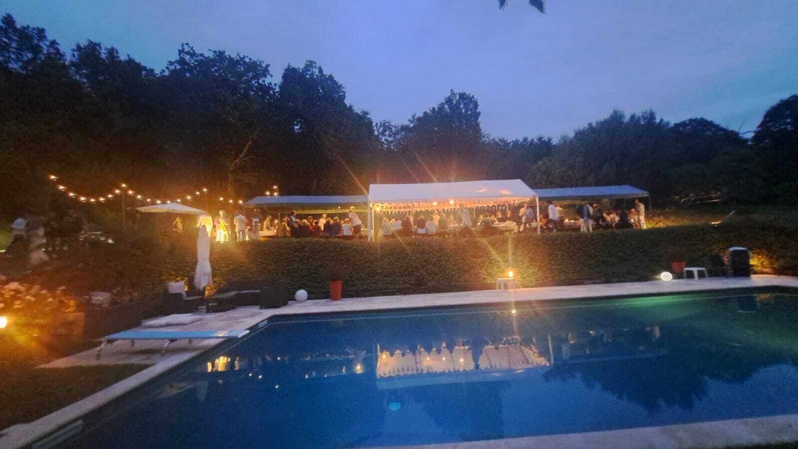 Un área de piscina con un espacio para fiestas cubierto por una carpa y luces colgantes.