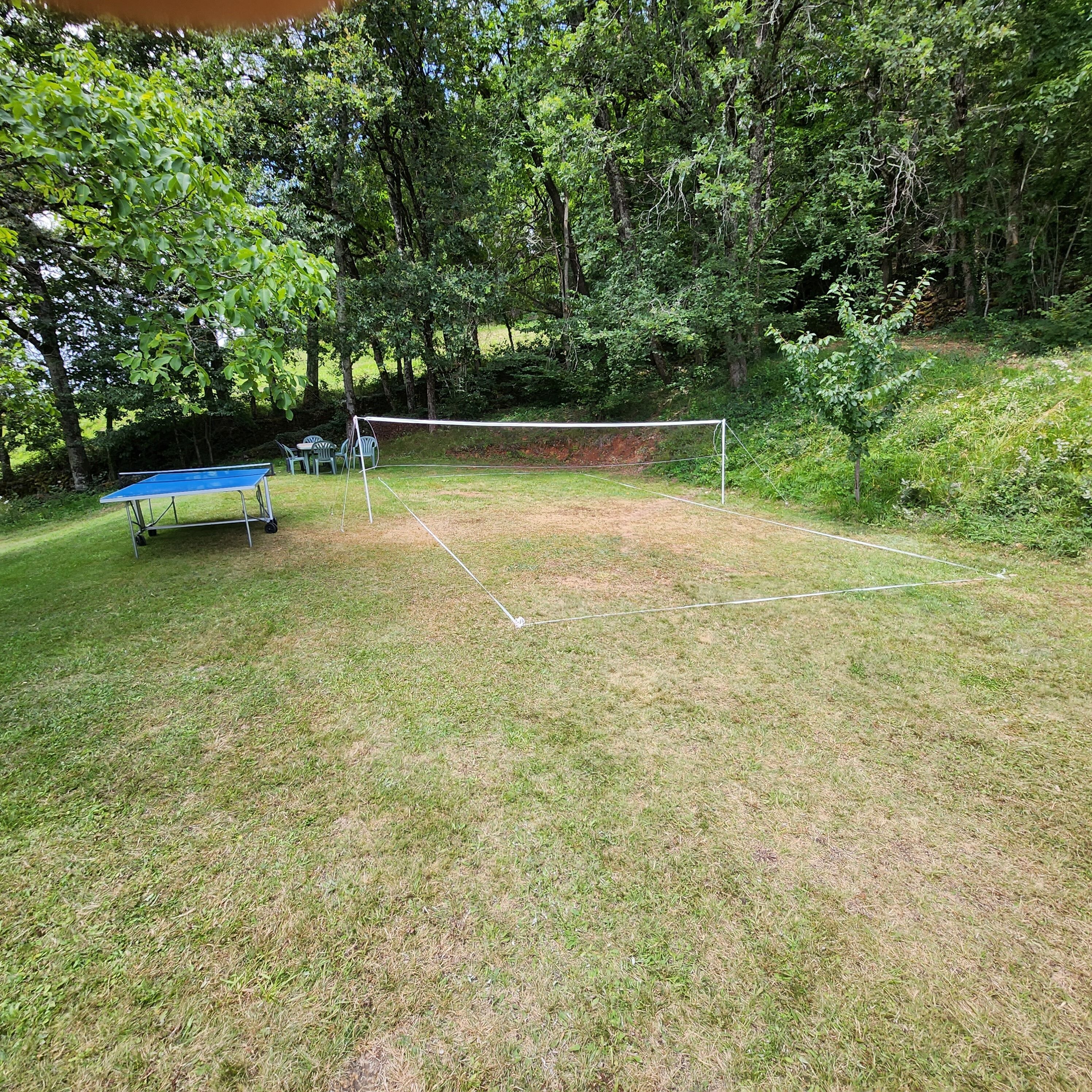 Ein Rasenplatz mit einem Badmintonnetz, einem blauen Tischtennis-Tisch und grünen Stühlen.