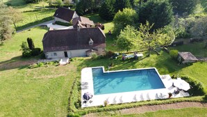 Vista aérea de uma propriedade com piscina, casa de pedra e gramado bem cuidado.