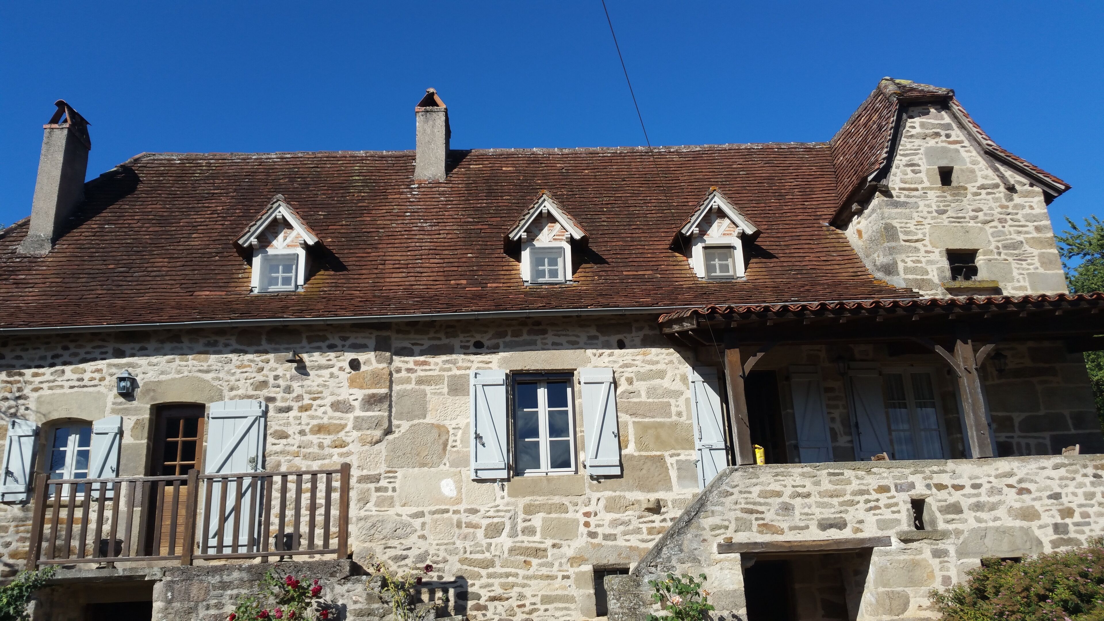 A stone building with a tiled roof, multiple chimneys, and a balcony with a railing.