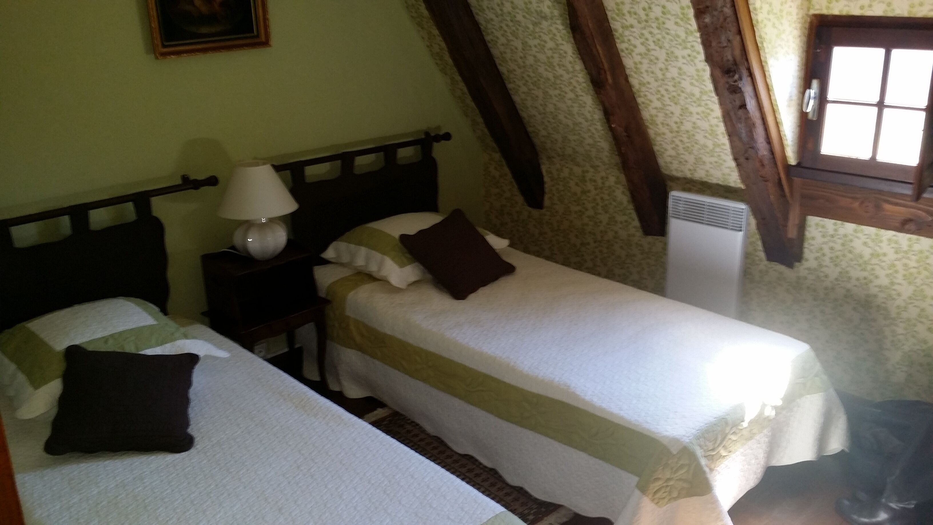 A bedroom with two beds, a nightstand with a lamp, and a window with a view of the outside.