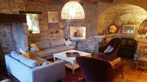 Um quarto aconchegante com parede de pedra, teto de madeira, um sofá, uma poltrona, mesa de centro e lareira.