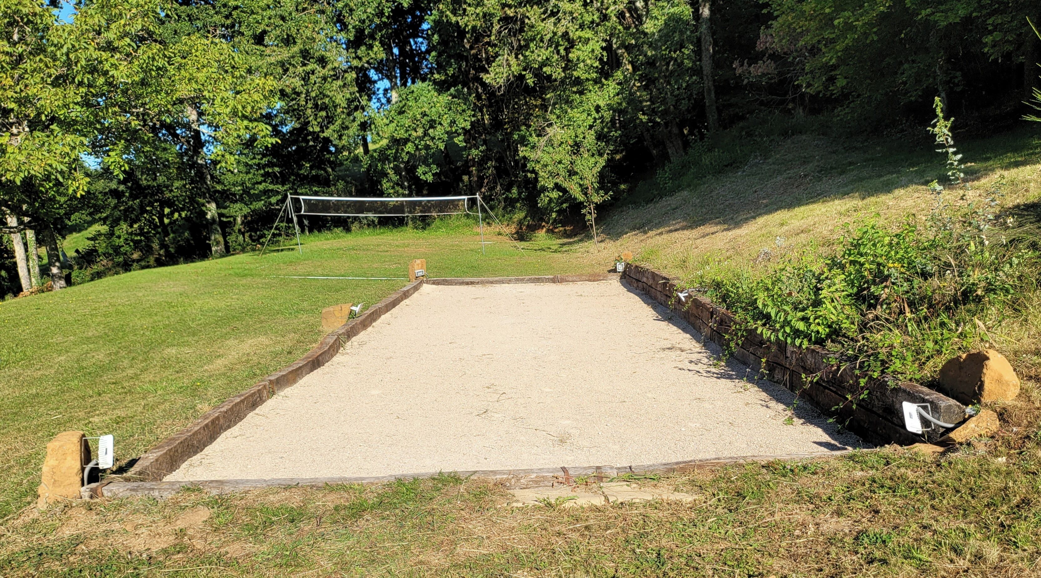 A volleyball court with a net, surrounded by grass and trees.