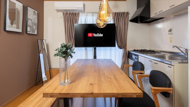 A modern kitchen with a wooden dining table, a hanging light fixture, a flat-screen TV, and a stove. - Maison Raffine (Osaka)