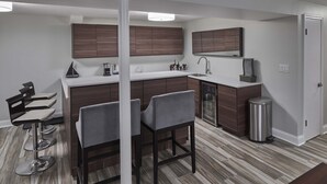 A modern kitchen with dark wood cabinets, a white countertop, and a stainless steel sink. There are three bar stools and a refrigerator with a Heineken logo. - Funtana Home for 8 (Fontana)
