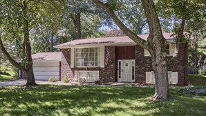 A two-story brick house with a garage, surrounded by trees and a well-maintained lawn. - Funtana Home for 8 (Fontana)