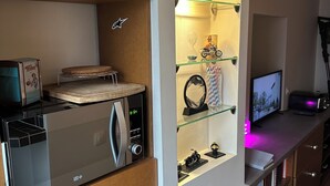 Een moderne keuken met een ingebouwde magnetron, een koelkast en een glazen schap waarop decoratieve spullen staan.