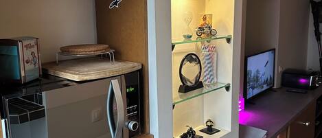 A modern kitchen with a built-in microwave, a refrigerator, and a glass shelf unit displaying decorative items.