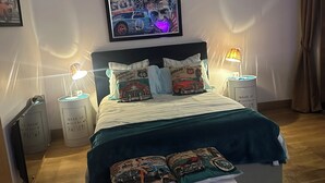 Een slaapkamer met een bed, twee nachtkastjes, een hoofdbord, een aan de muur hangend schilderij en een bedlamp.