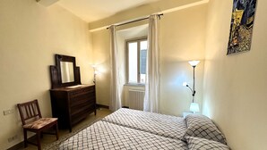 Ein Schlafzimmer mit Bett, Kommode, Stuhl und einem Fenster mit Vorhängen.