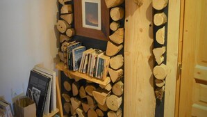 A room with a wall decorated with stacked logs, a bookshelf, and a framed picture. - Gite for two people Le frêne (Rosay)