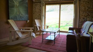 A room with a glass-top table, two white rocking chairs, a red rug, and a stone wall. - Gite for two people Le frêne (Rosay)