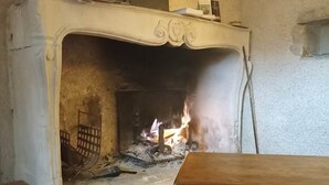 A fireplace with a fire, a bench, and a wall with a picture frame. - Gite for two people Le frêne (Rosay)