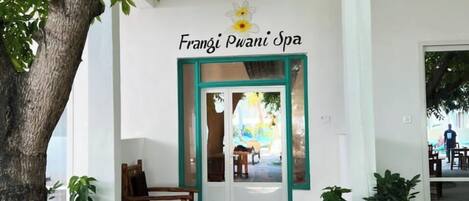 A spa entrance with a sign reading 'Frangzi Pwani Spa,' a wooden bench, potted plants, and a view into the spa area.