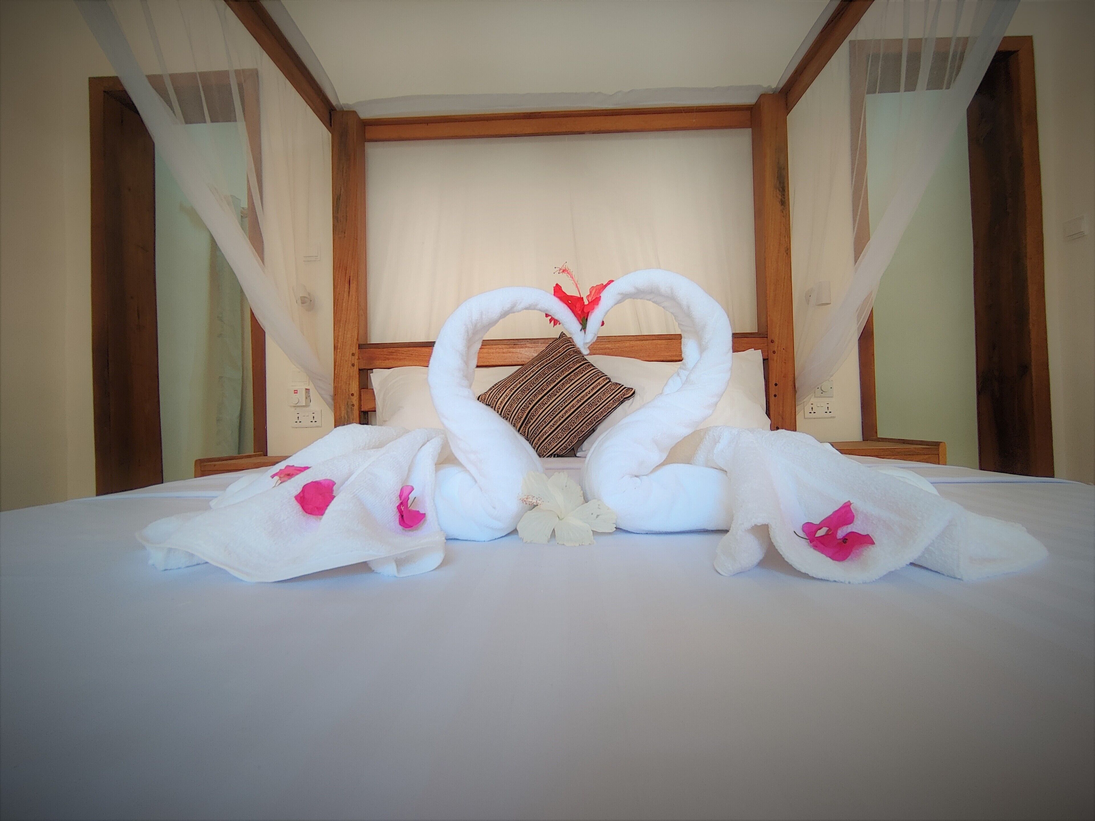 A hotel room with a bed, a wooden headboard, and a decorative swan towel arrangement.