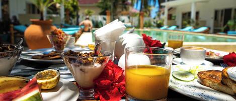 A breakfast setting with various dishes, a glass of orange juice, and a poolside view.
