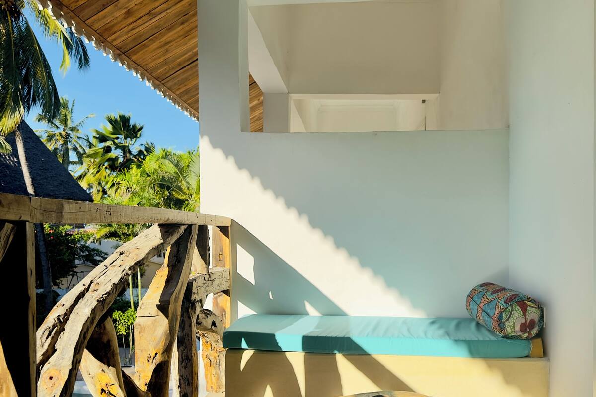 Une terrasse en bois avec un banc et une table, donnant sur une piscine et des palmiers.