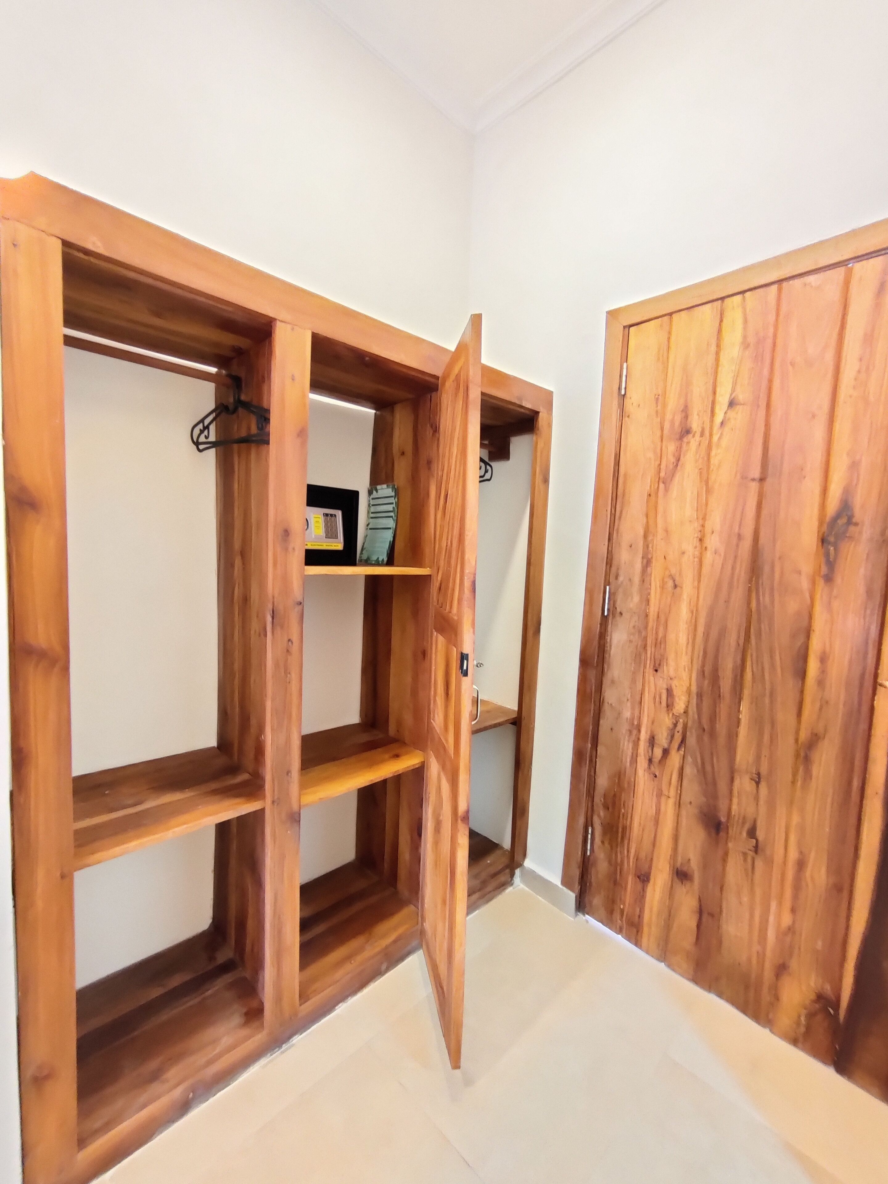 Une armoire en bois, dont les portes sont ouvertes, laissant apparaître des étagères et un espace pour suspendre des vêtements.