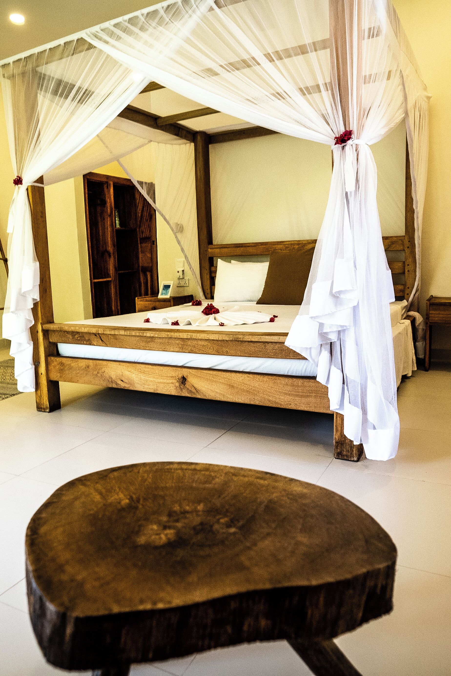A wooden bed with a canopy, a wooden bench, and a wooden door in the background.
