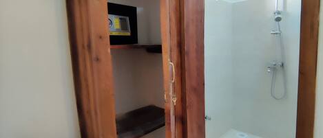 Puerta de madera que da a un área de ducha con un cabezal de ducha manual y un panel de control en la pared.