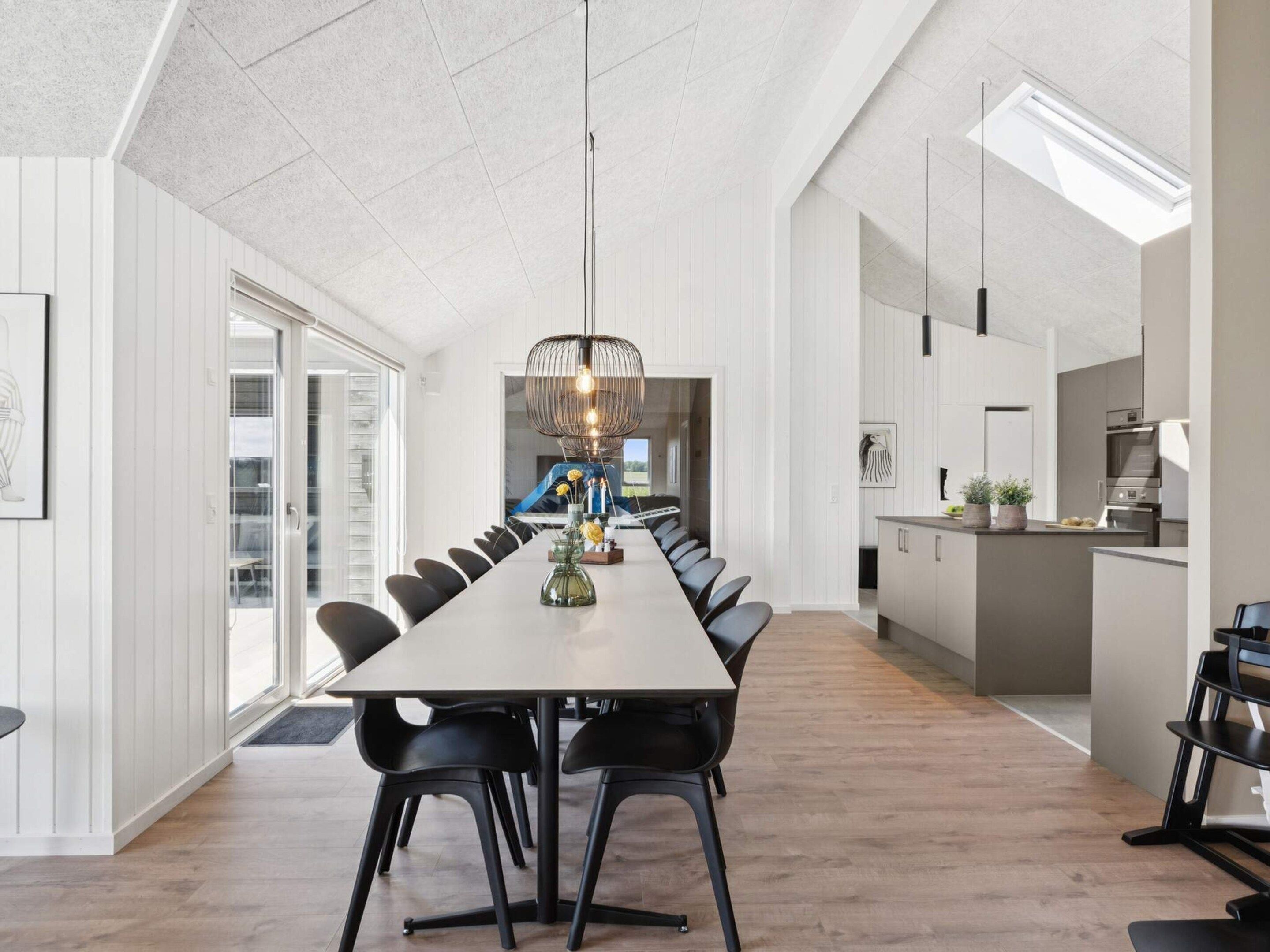 A modern dining area with a long table, black chairs, and a unique pendant light.