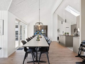 A modern dining area with a long table, black chairs, and a unique pendant light.