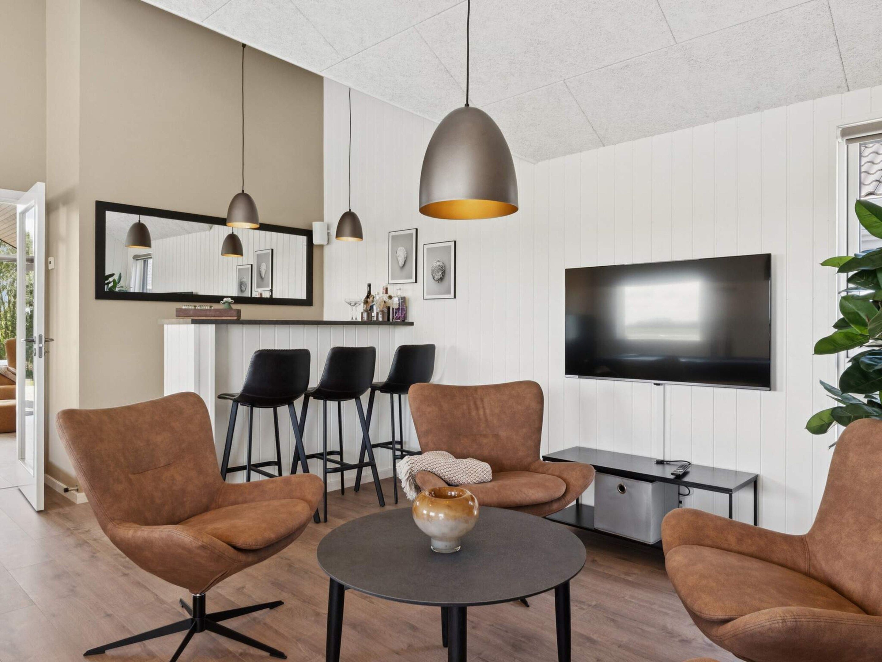 A modern living room with a TV, comfortable seating, and pendant lighting.