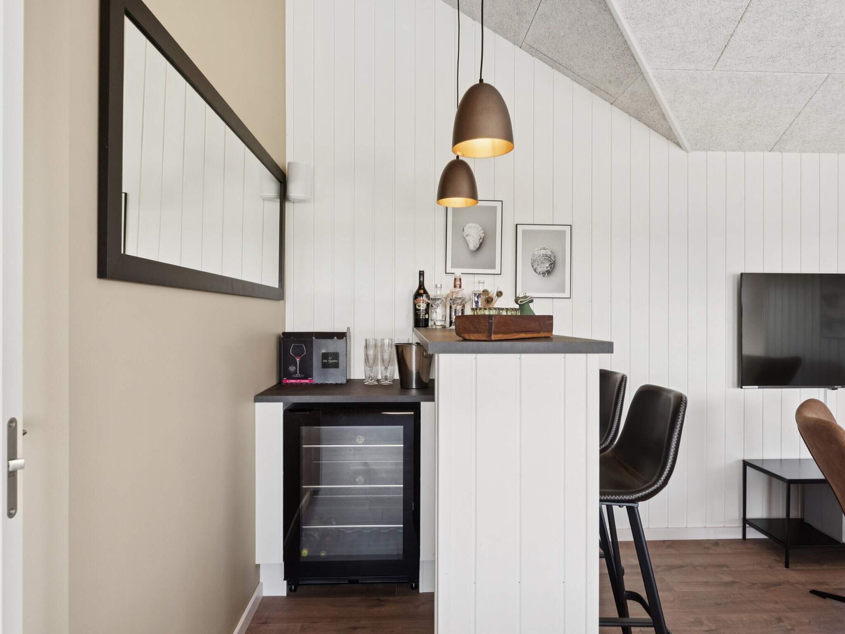Una cocina moderna con un refrigerador empotrado, una zona de bar con vasos y botellas, y un televisor montado en la pared.