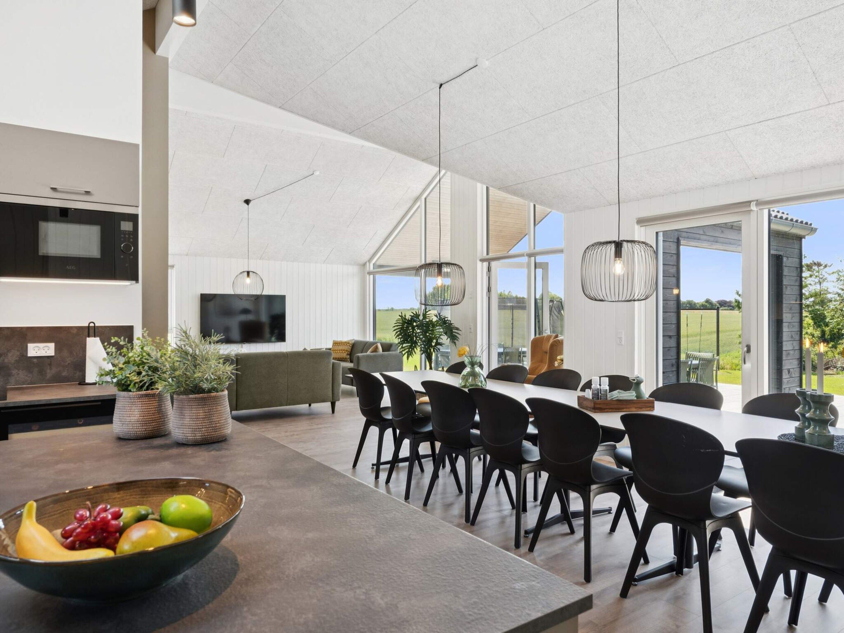 A modern kitchen with a dining area, large windows, and a fruit bowl on the counter.
