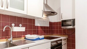 Una cocina con un lavamanos de acero inoxidable, armarios blancos, un microondas y un salpicadero con azulejos rojos.
