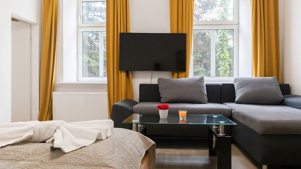 Una habitación de hotel moderna con sofá, una mesa de centro de vidrio, televisor de pantalla plana y ventana con cortinas.