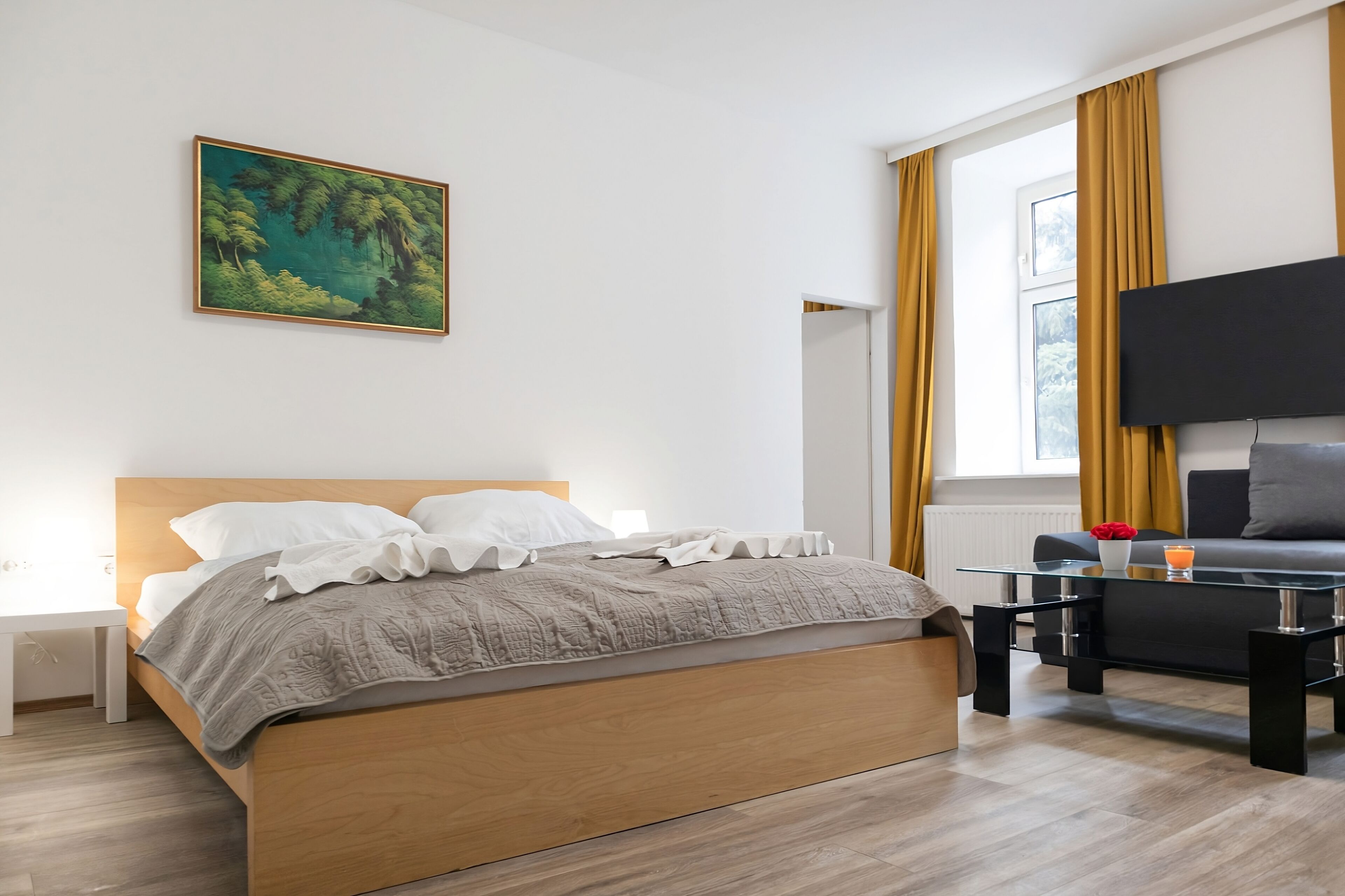 A modern bedroom with a wooden bed, a glass coffee table, a sofa, and a painting on the wall.