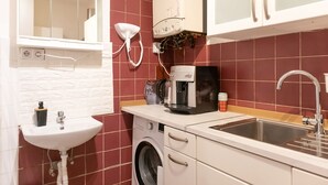 Una cocina compacta con lavadora, cafetera, lavabo y espejo.