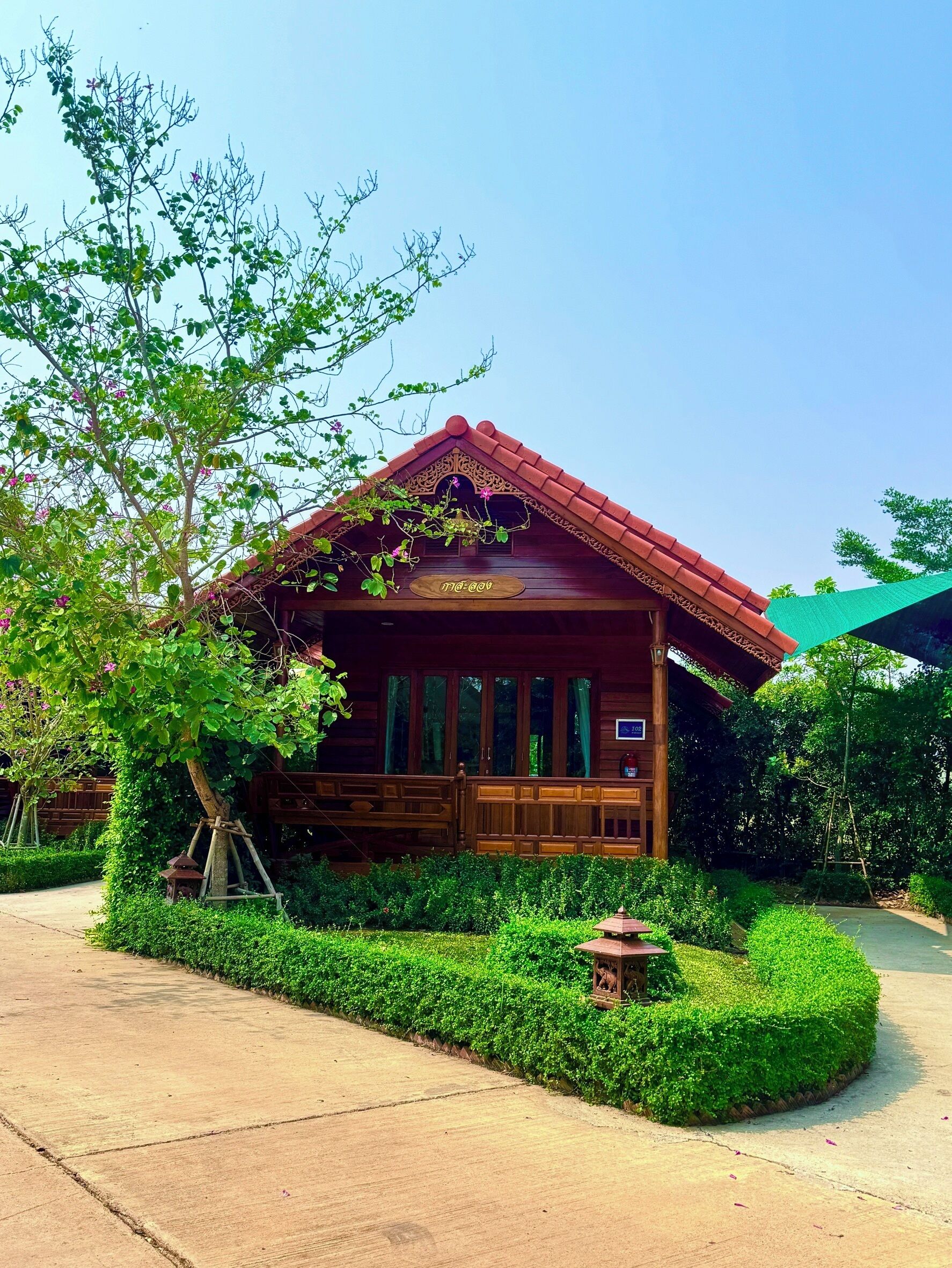A wooden cabin with a red roof, surrounded by lush greenery and a clear sky.
